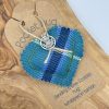 A heart-shaped tartan fabric in vibrant red and blue hues, featuring a delicate silver charm, is elegantly tied with twine to a rustic brown tag. The tag proudly displays the message, Wee Tartan Hug: Delivering a Scottish embrace wrapped in authentic tartan. This charming set makes a perfect addition to any collection and rests beautifully on a classic wooden surface. Ideal for those seeking unique Scottish gifts or traditional tartan-inspired decor.