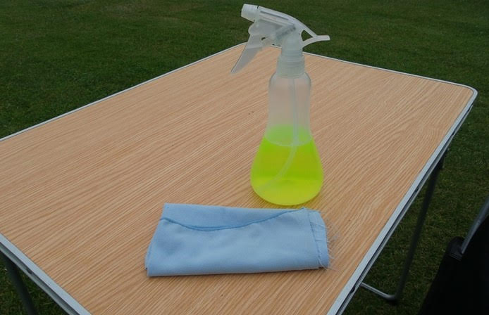 Een plantenspuit gevuld met allesreiniger en water staat op een kampeertafel.
