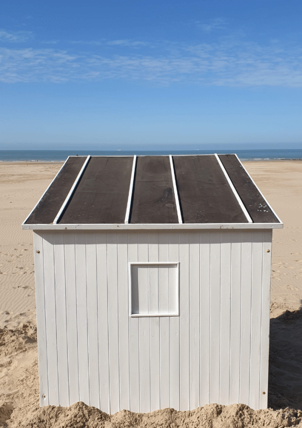 Een witte strandcabine staat op het strand. Op de achtergrond zie je de zee.