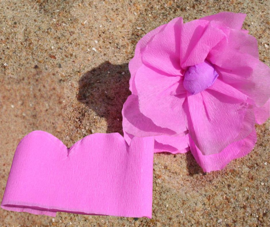 Een roze bloem met hoe de bloemblaadjes uit crepepapier geknipt moeten worden.