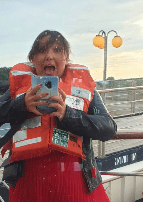Bij een cruise hoort ook een verplichte reddingsoefening. Op de foto zie je een vrouw in galakledij met een reddingsvest aan, op het dek van een cruiseschip.