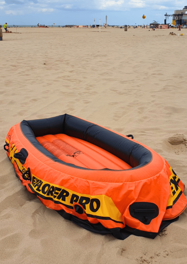 Een oranje opblaasbootje is kapot en ligt klaar op het strand om te herstellen.