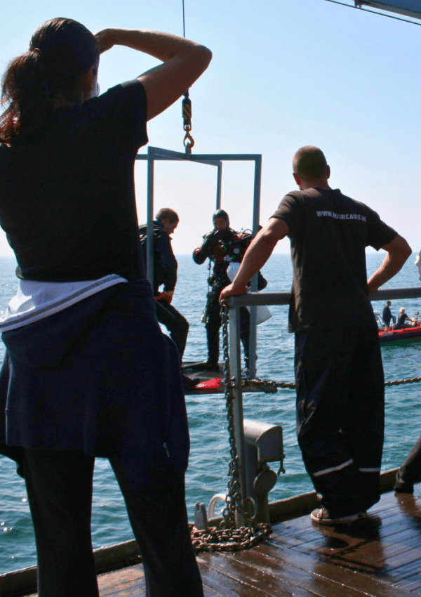 Twee duikers staan klaar op een lift om aan boord van het schip gehesen te worden.