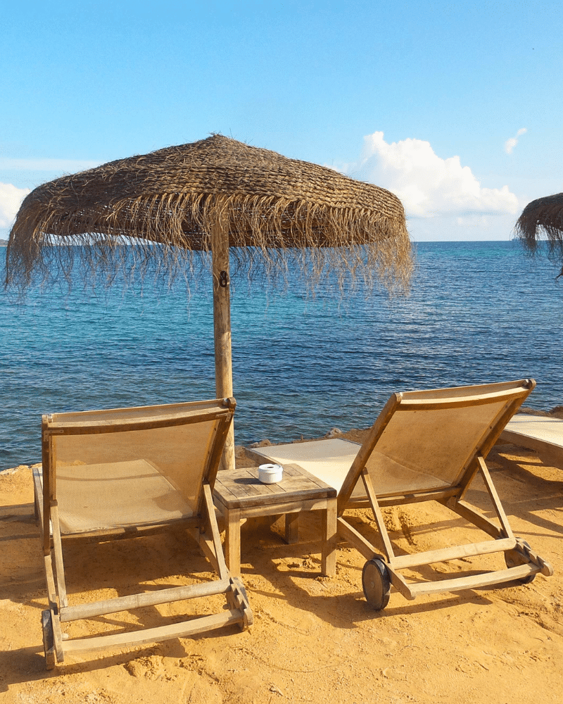 Strandclub in Ibiza met ligzetels en een rieten parasol aan het water.