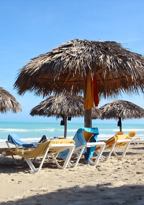 Een strandje in Varadero, Cuba, met ligzetels en strooien parasols, bij de zee.