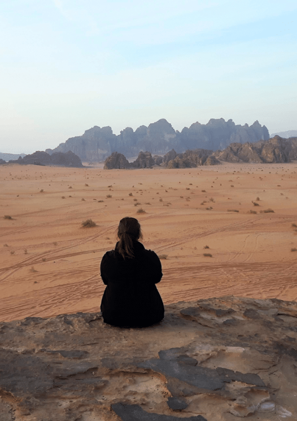 Een dame met een zwarte fleece aan kijkt uit over een woestijnlandschap in Wadi Rum in Jordanië.