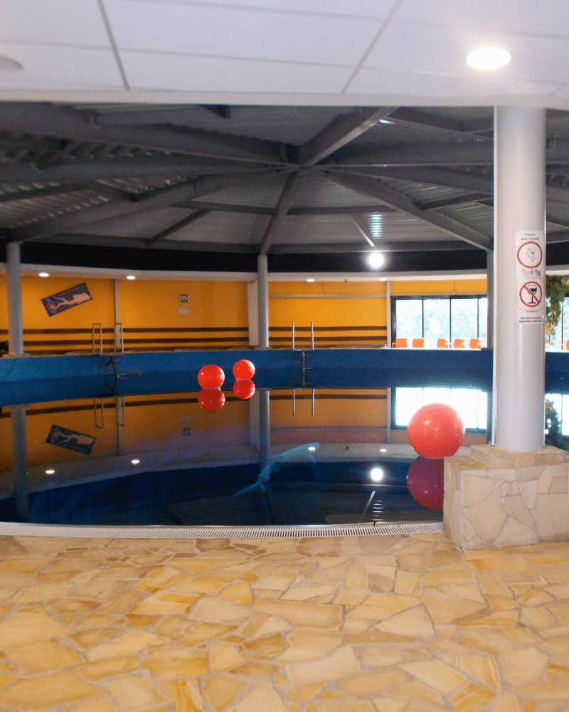 Het indoor duikcentrum Dive4life in Duitsland. Er liggen oranjerode boeien op het water. De muren zijn geel geverfd. 