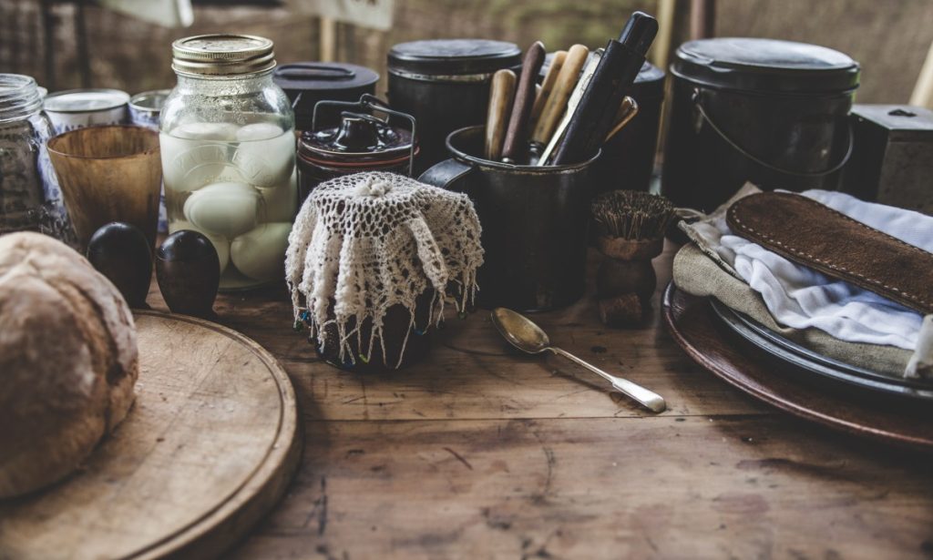 A homesteader's kitchen counter full of food containers, bread, cutlery and jars.