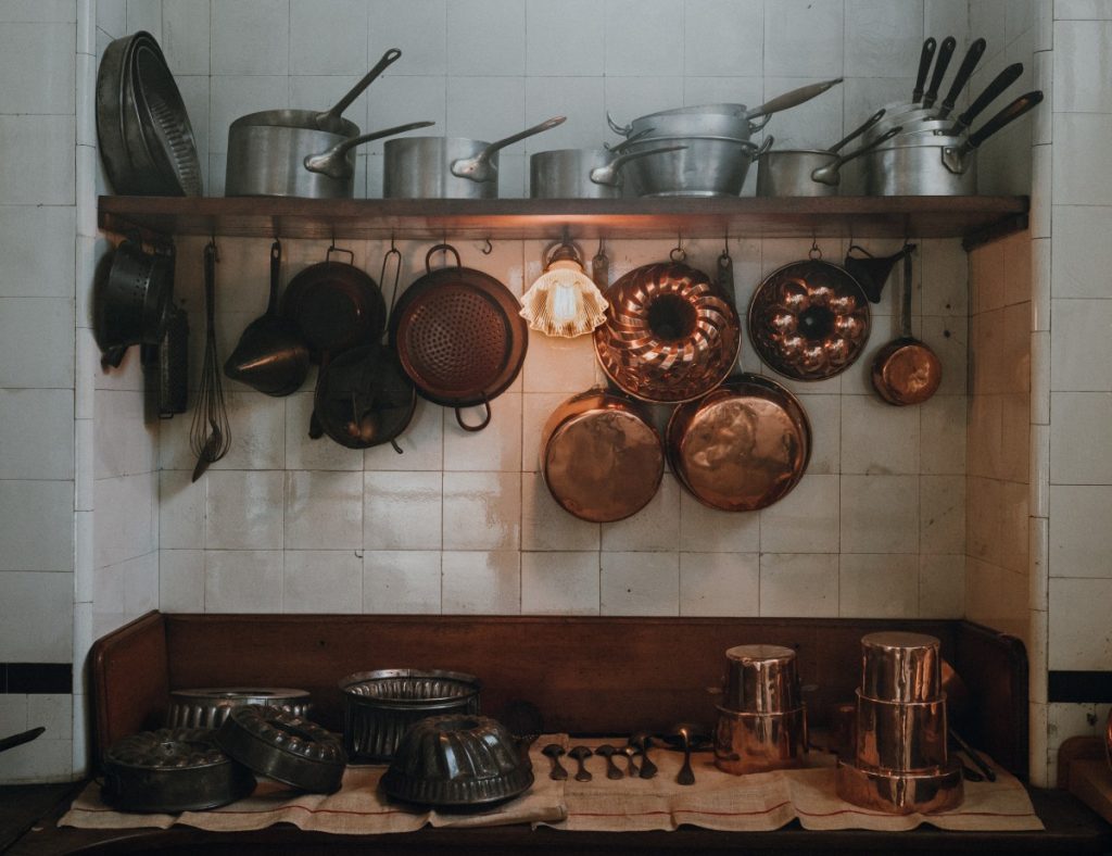 A beautiful, traditional kitchen with lots of copper pots and pans hanging from a shelf above a kitchen counter. You don't have to have an old fashioned wood burner to get started home steading. 