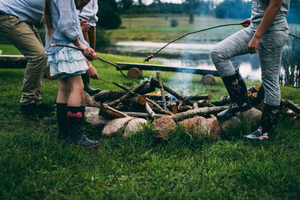 Kid and adults standing around a fireplace with sticks into the fire - perhaps marshmellows