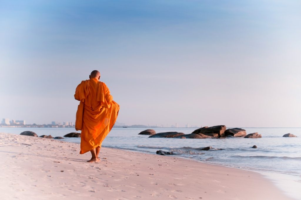 Monk walking on a beach. Meditating is a way to practice yoga.