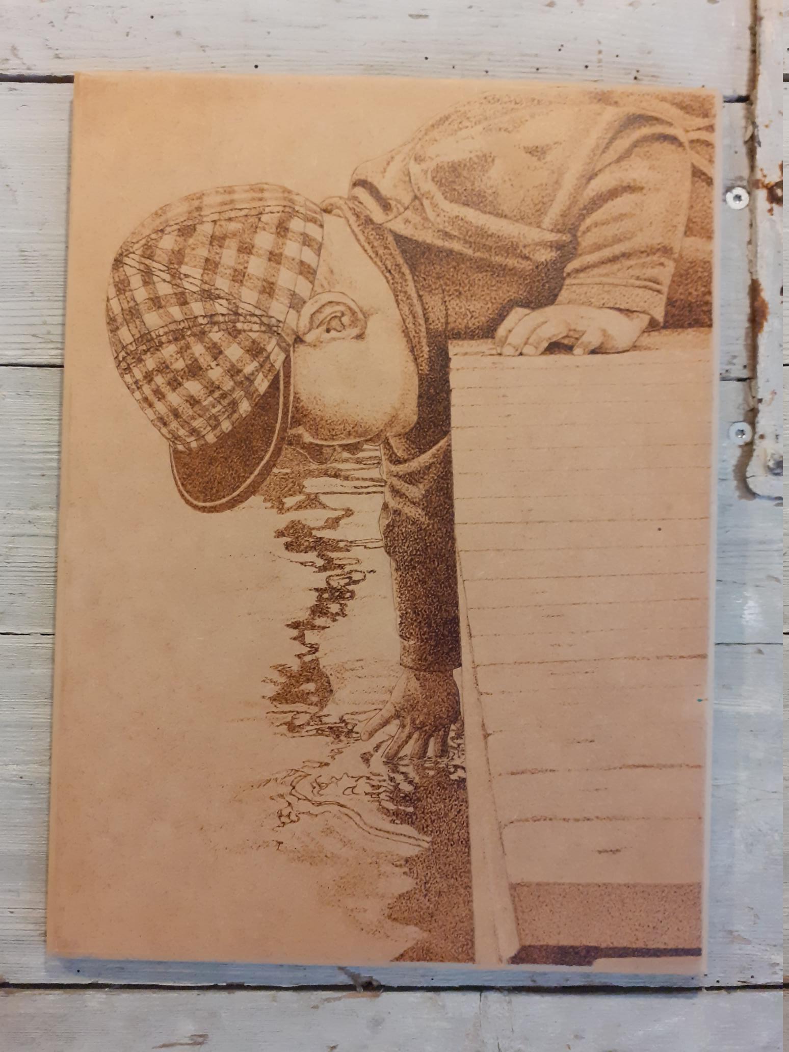 trätavla med glödritat motiv, liten pojke som ligger på en brygga och sträcker ner handen till vattnet