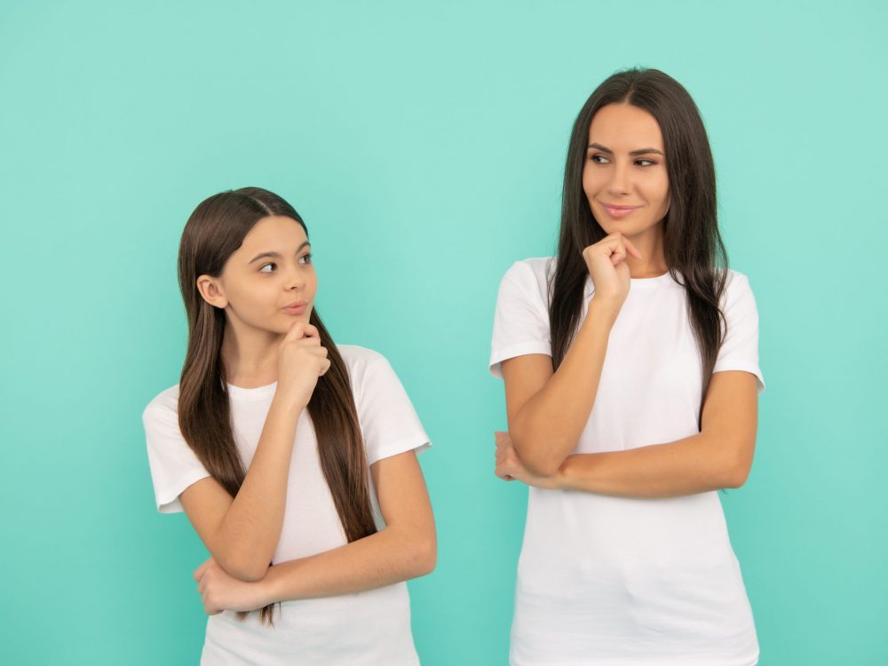 Thoughtful mother and daughter with pensive look keep hands on chin blue background, imagination.