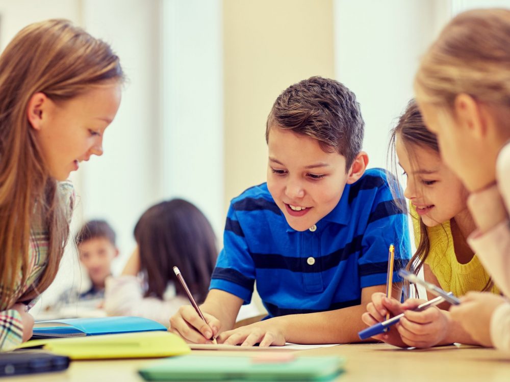 education, elementary school, learning and people concept - group of school kids with pens and papers writing in classroom