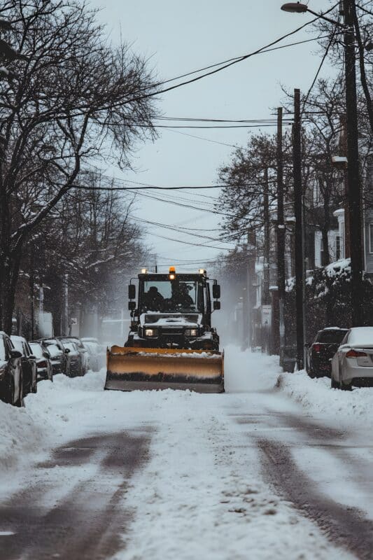 snow plow is driving down street with snow ground