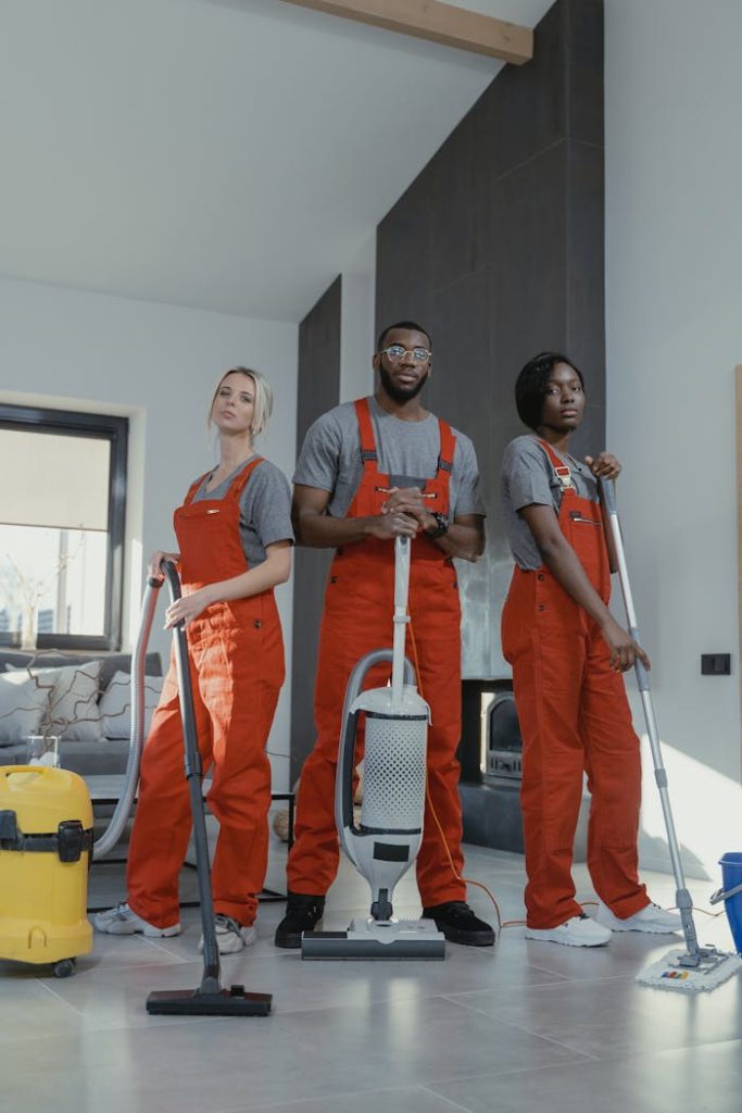 man-in-red-polo-shirt-beside-woman-in-blue-polo-shirt-6195131 Three cleaners in uniform with equipment in a modern home interior, showcasing teamwork and professionalism.