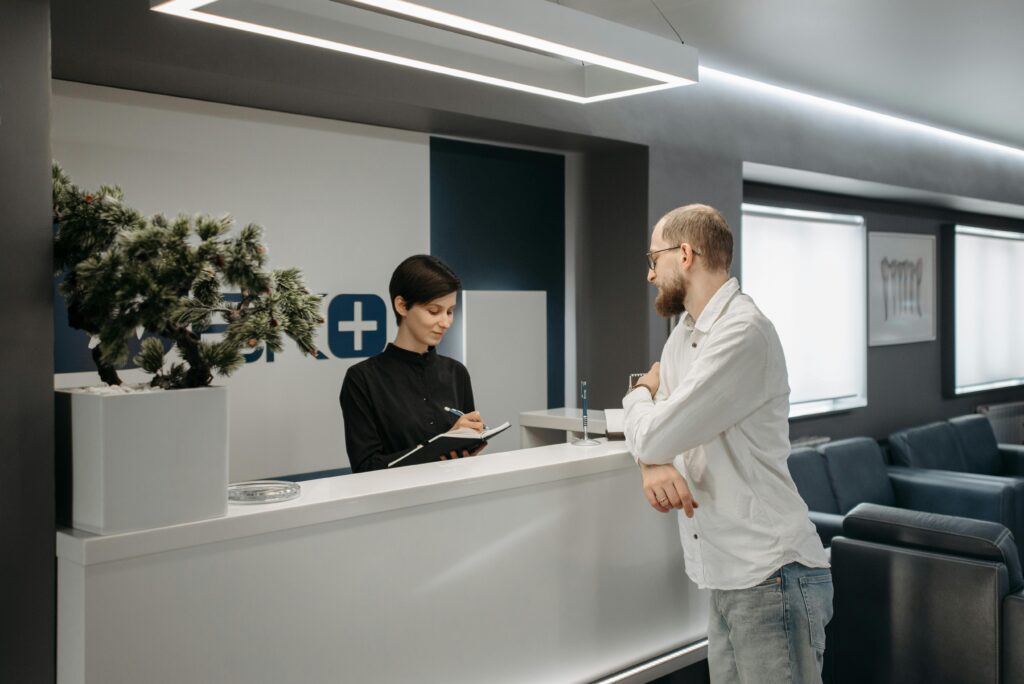 pexels-photo-6809658-6809658 A man consults a receptionist in a modern clinic setting with contemporary design.