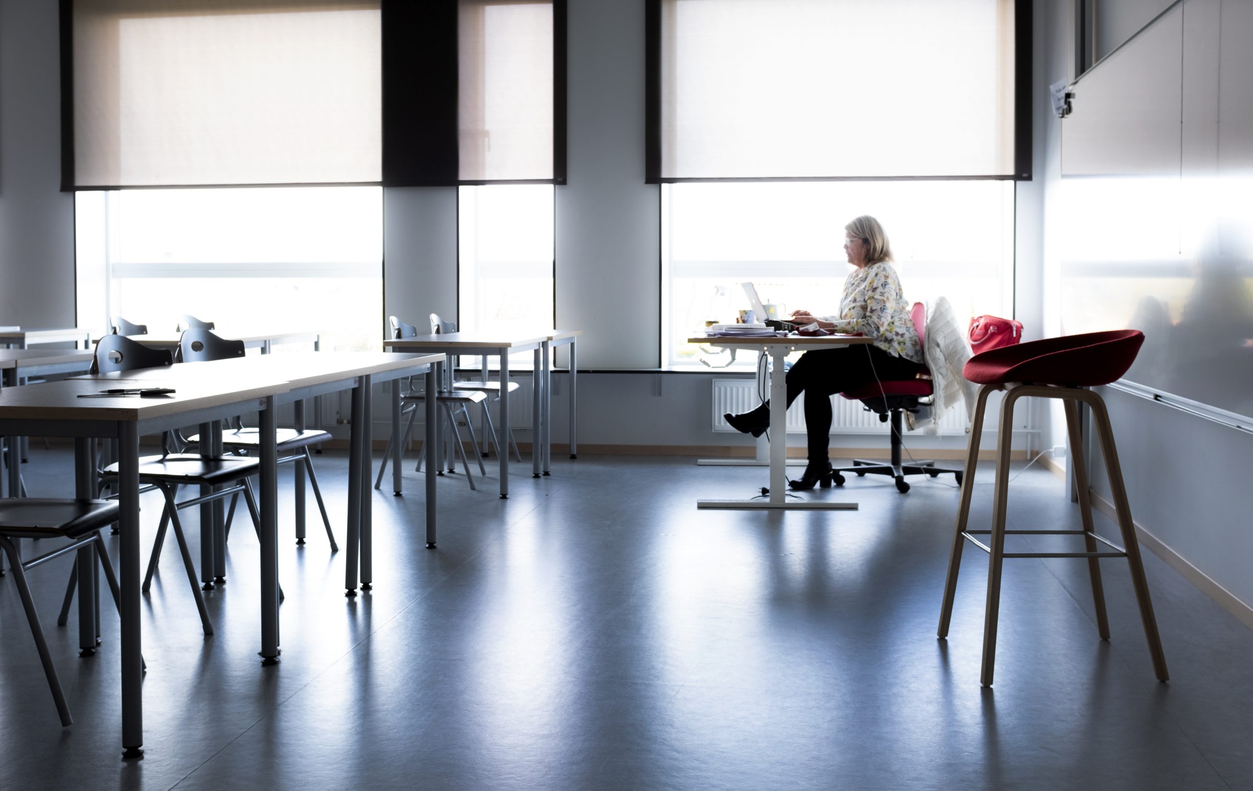 En lärare sitter själv vid en dator, i ett tomt klassrum