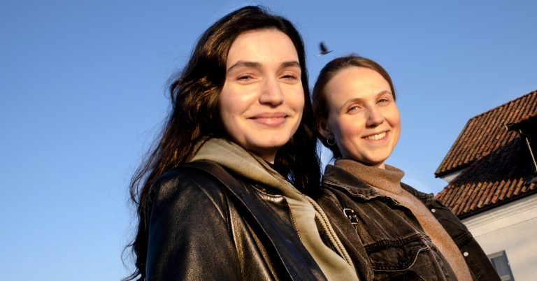 Två unga kvinnor går arm i arm och ser glada ut