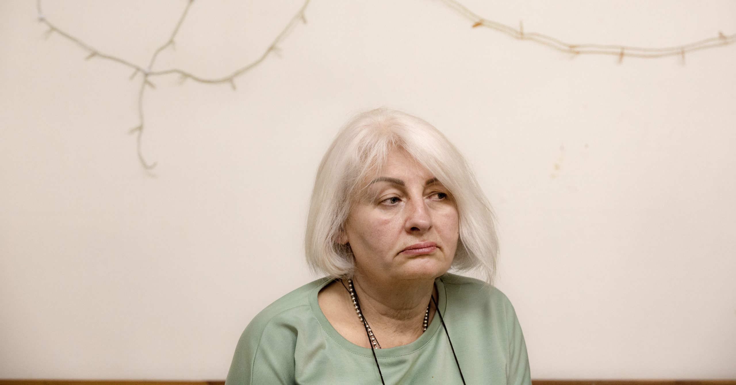 En äldre kvinna med vitt hår och ljusgrön tröja ser ledsen ut