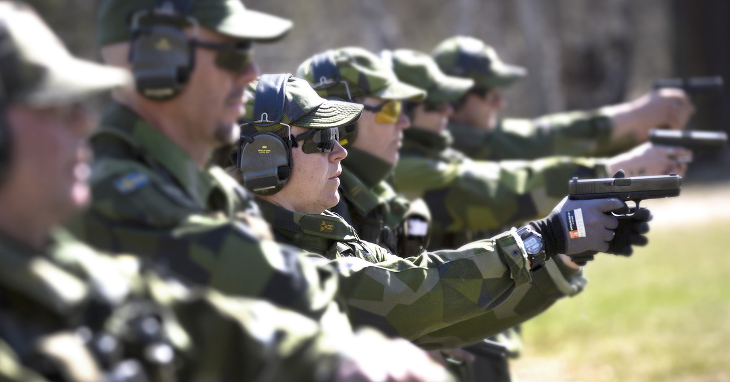 Människor i militära kläder står på rad med dragna pistoler
