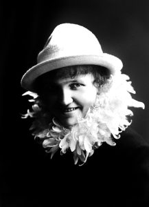 En svartvit bild av en ung kvinna med hatt och fjäderboa runt halsen