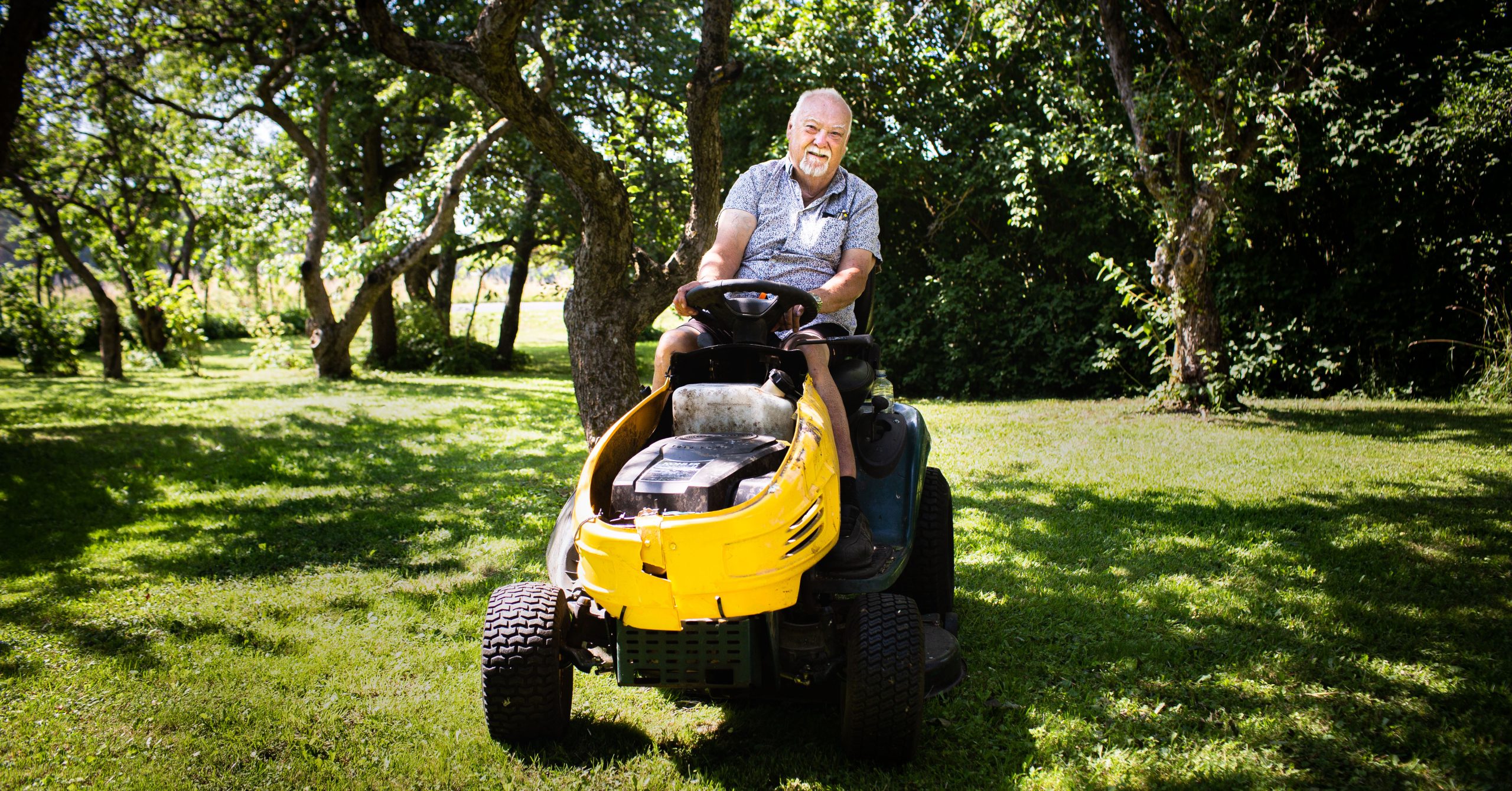 En glad äldre man på en gul åkgräsklippare