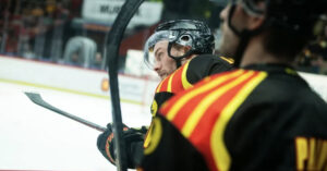 En hockeyspelare sitter med full mundering på en bänk och tittar ut över isen