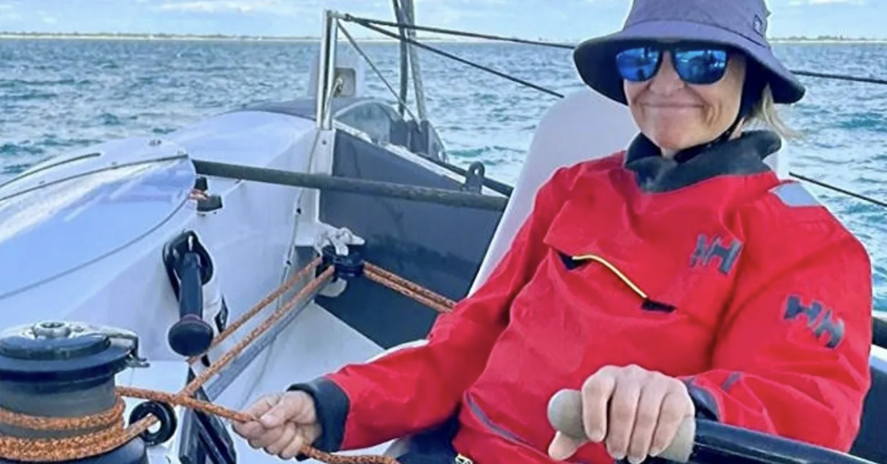 En glad kvinna med solglasögon sitter i en segelbåt
