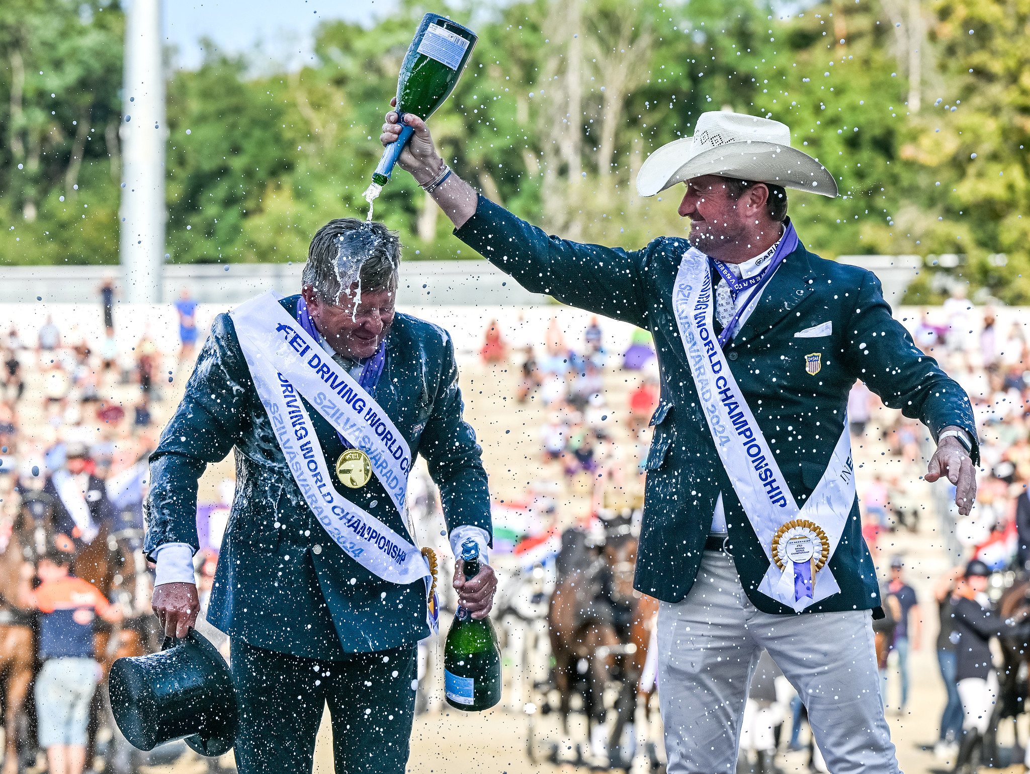 Bronze CHESTER WEBER aus den USA gießt Champagner über den goldenen BOYD EXELL aus Australien nach der FEI-Weltmeisterschaft im Vierspännerfahren in Szilvásvárad, Ungarn, am 8. September 2024. Copyright FEI/Martin Dokupil