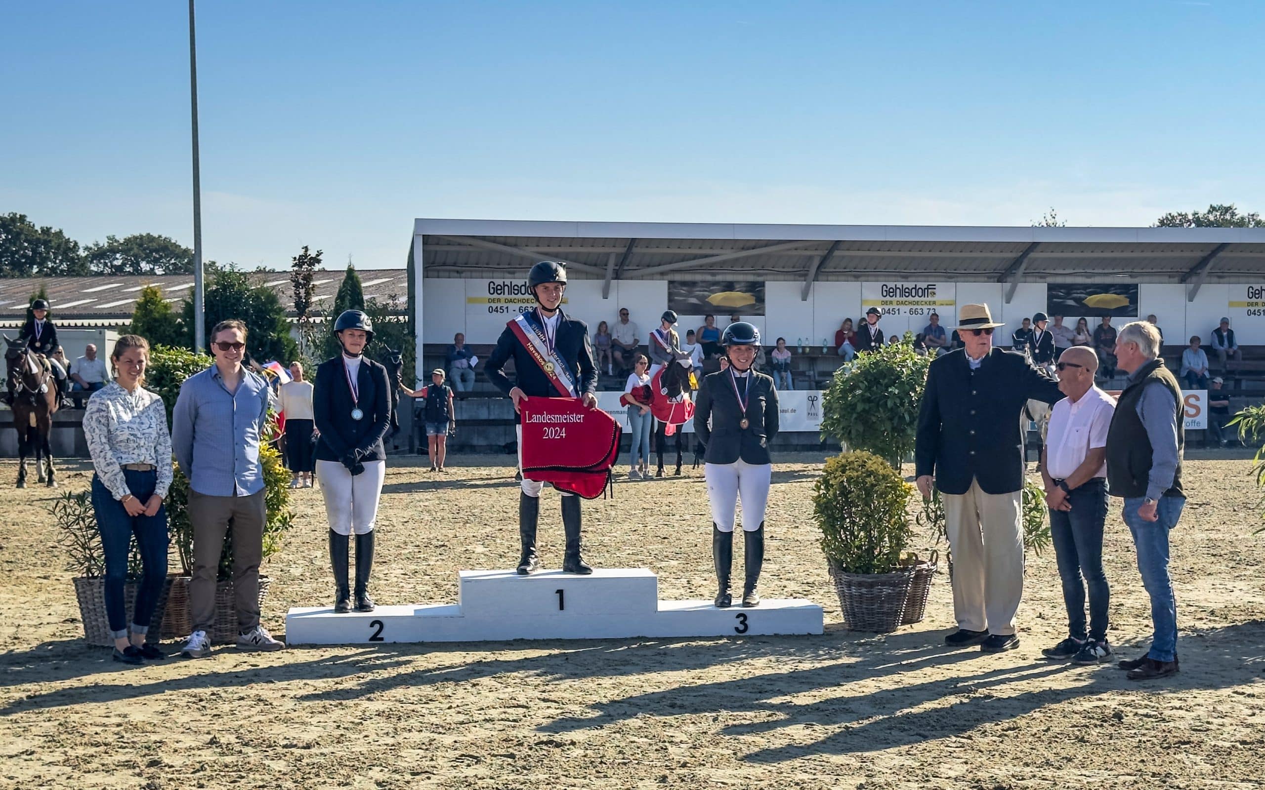 Auf´s Podest gejumpt sind Landesmeister Mathies Rüder, Zoé Neas (li.) Silber und Stina Struck (re.), Bronze. Zuvor gratulierten Sponsoren und der Vorsitzende des Pferdesportverband SH, Dieter Medow (3. v. re.). (Foto: photo-rocket)