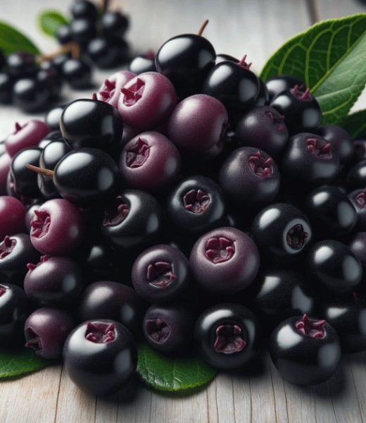 A handful of fresh Aronia berries, deep purple in color, placed on a light wooden table.