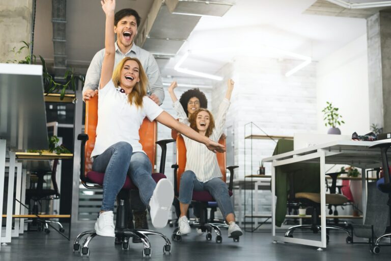 Overjoyed millennial colleagues racing on office chairs