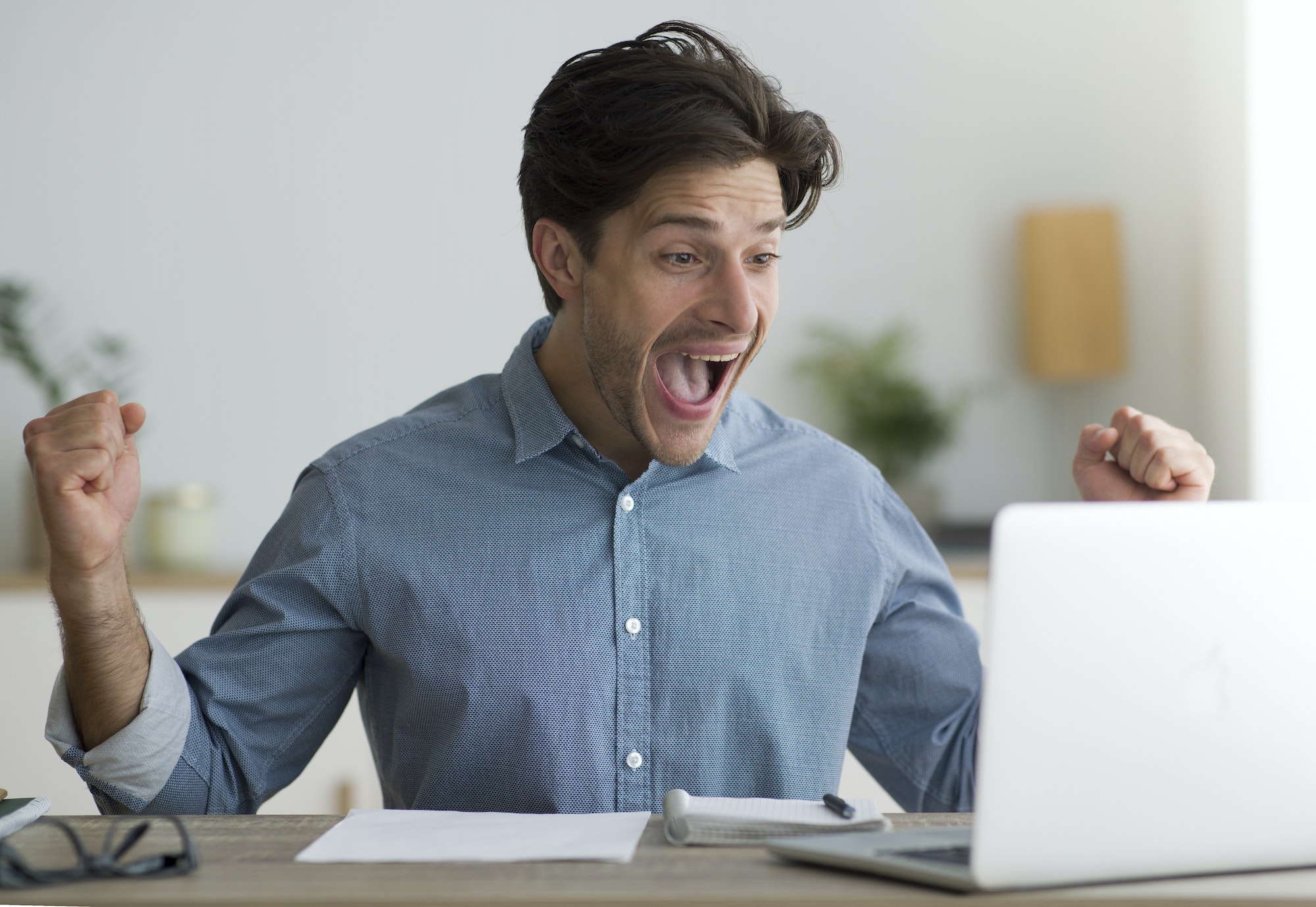 Guy Celebrating Success At Laptop Shaking Fists At Workplace