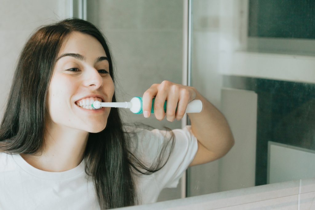 A young woman with black hair brushing his teeth with an electrical toothbrush