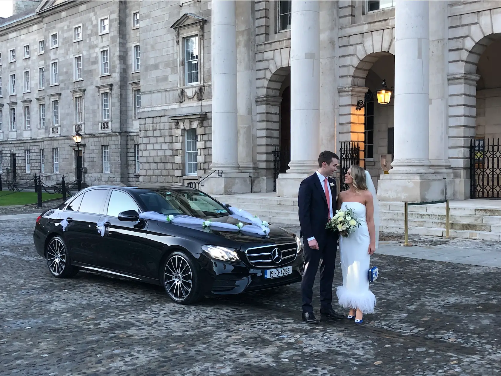 Bride and groom by wedding car.