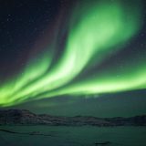 The northern lights shining bright above the frozen Ilulissat Icefjord