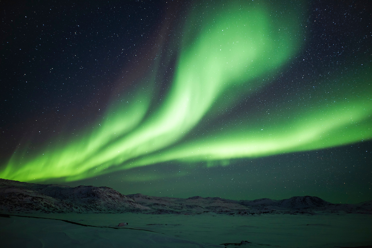 The northern lights shining bright above the frozen Ilulissat Icefjord
