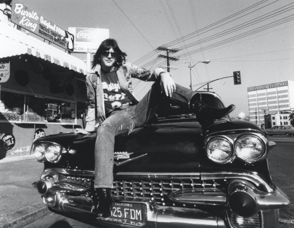 Personajes singulares y sus coches: Gram Parsons posa para promocionar su banda Flying Burrito Bros sentado sobre el capó de un Cadillac en Los Ángeles en 1971 | Ginny Winn : Michael Ochs Archives : Getty Images