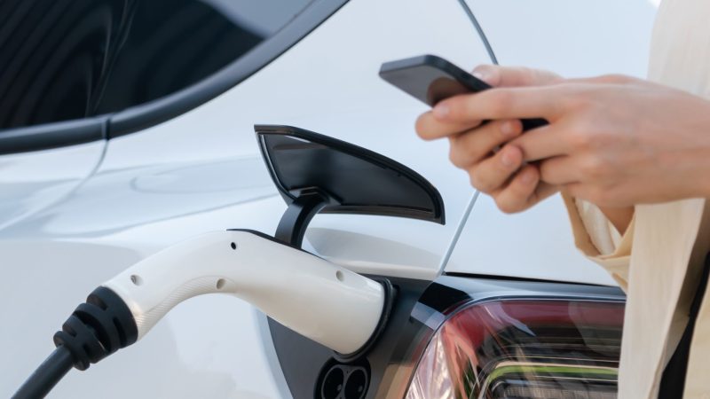 Young woman use smartphone to pay for electricity for EV car.