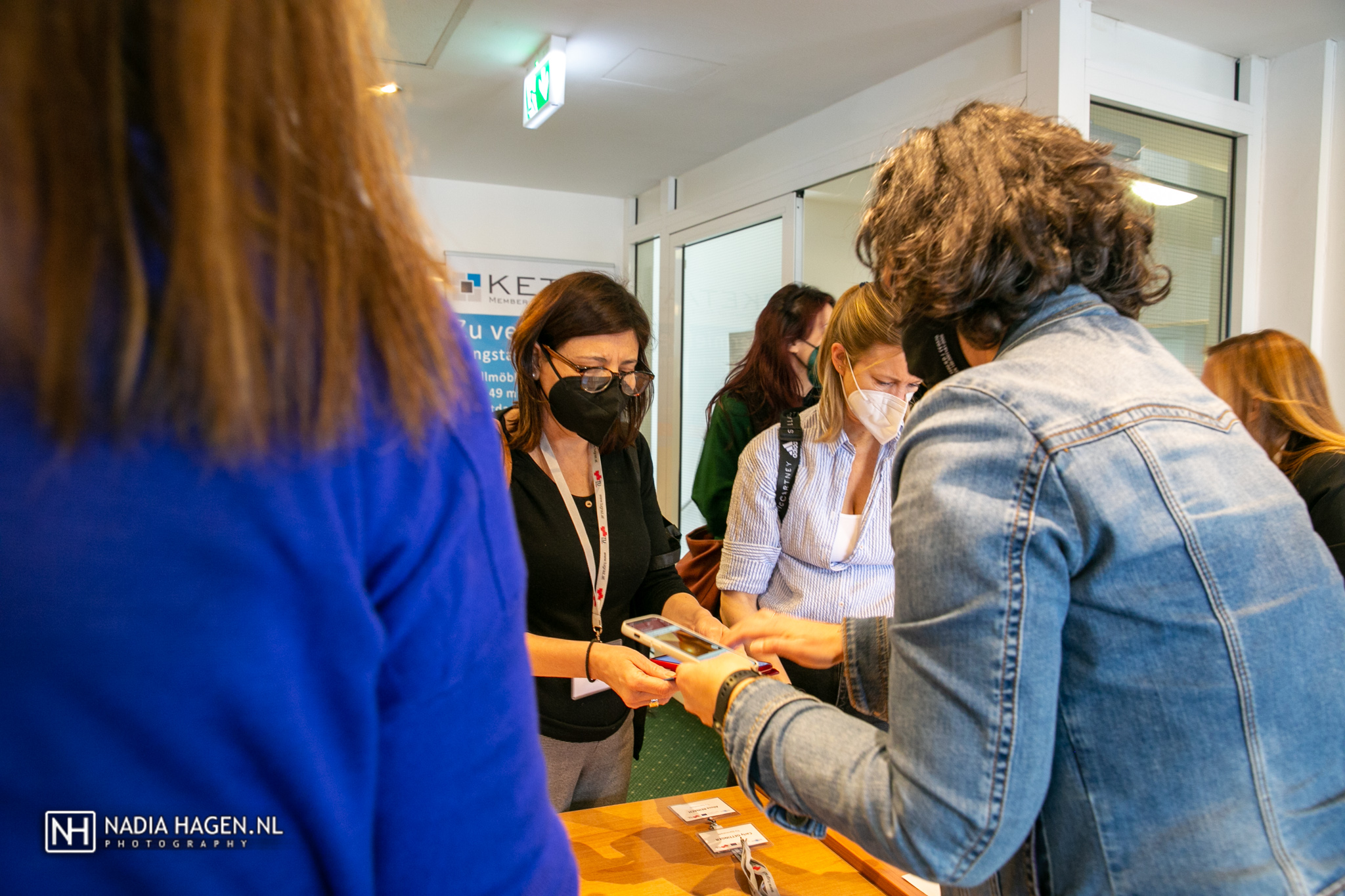 a woman in a black medical face mask shows her phone to another woman.