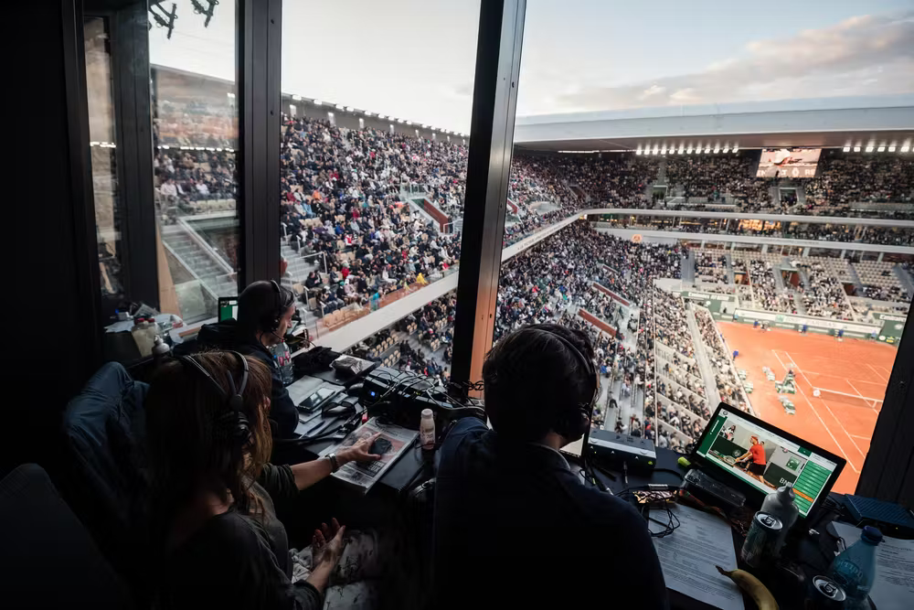Imagen de los comentaristas en la cabina de Radio Roland Garros supervisando la cancha del estadio Philippe Chatrier.