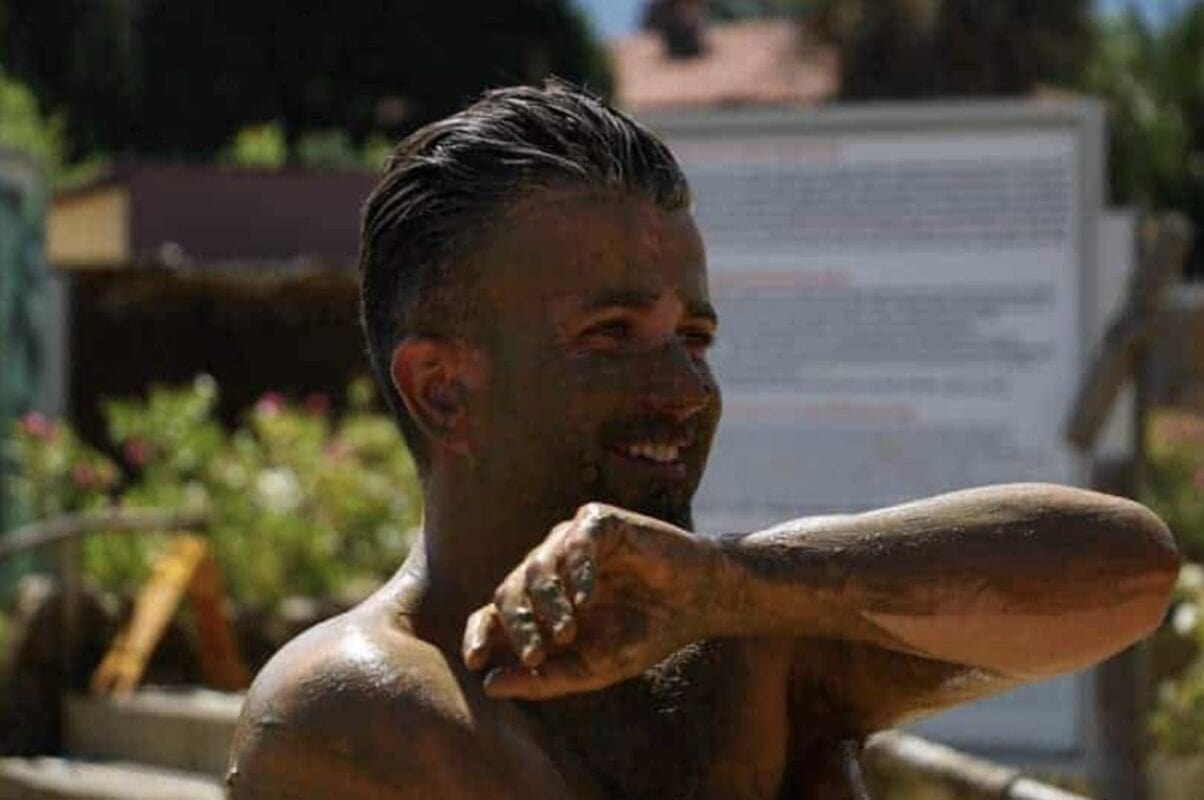 Man applying mud to his arm, smiling in the sun at the Mud Baths in Dalyan