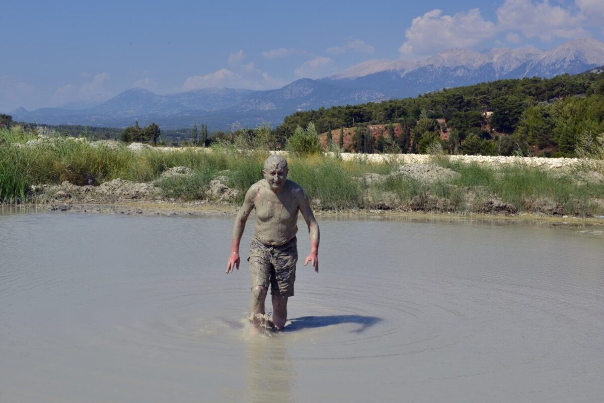 Man standing in a mud pool with a mountain backdrop