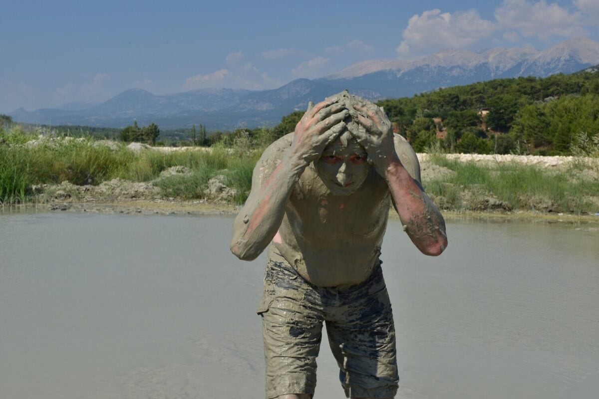 Person covered in mud with hands on their head, outdoors