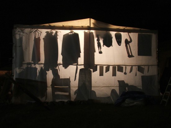 shapes and outlines of clothing and carvings silhouetted against a canvas stall