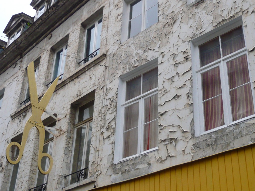 street sign in the form of a large pair of golden scissors, on a building facade with flaking paintwork