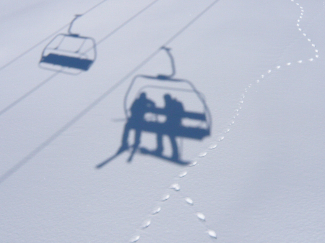 shadows of chairlift cast on snow and tracks of mountain hare on the snow surface