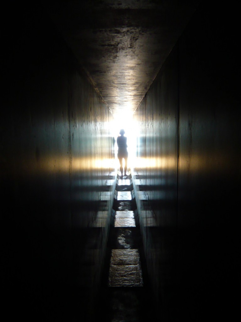 woman's silhouette against bright sunlight as she exists concrete lined passage