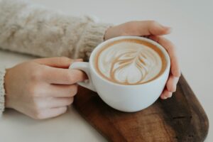 Coffee cup in a woman's hands sat on a piece of wood